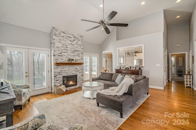 living room with ceiling fan, french doors, a stone fireplace, high vaulted ceiling, and light wood-type flooring