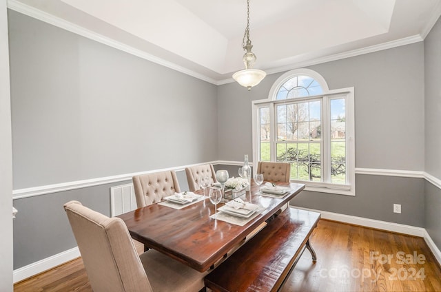 dining space featuring hardwood / wood-style flooring, a raised ceiling, and ornamental molding