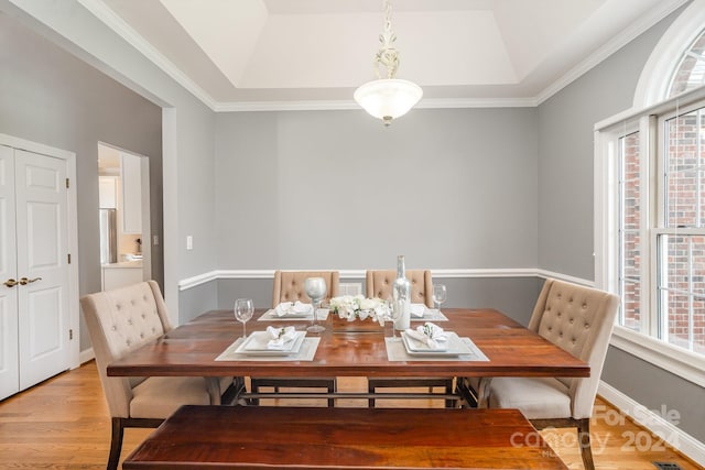 dining room featuring ornamental molding, a tray ceiling, light hardwood / wood-style flooring, and a healthy amount of sunlight