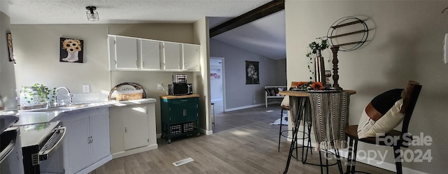 kitchen featuring white cabinets, lofted ceiling with beams, light wood-type flooring, a textured ceiling, and range