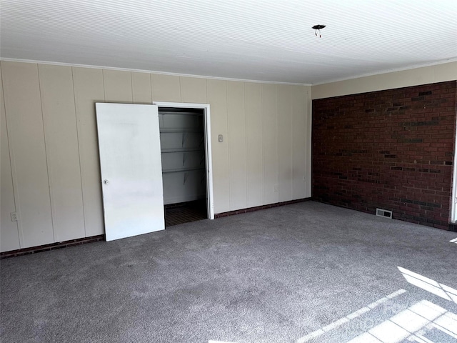 carpeted empty room featuring crown molding and brick wall