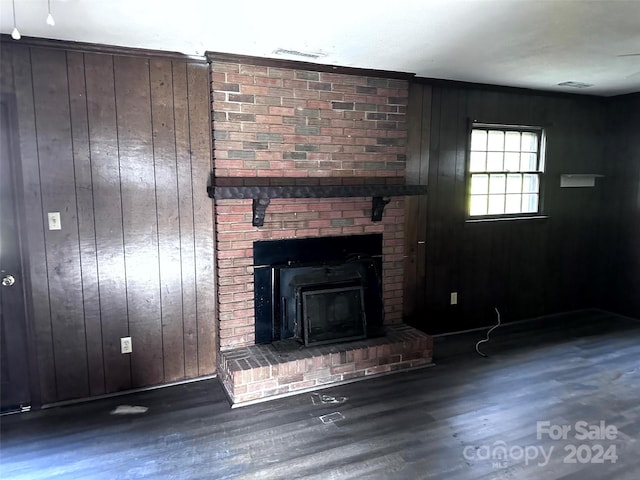 unfurnished living room with a wood stove, wooden walls, and dark wood-type flooring