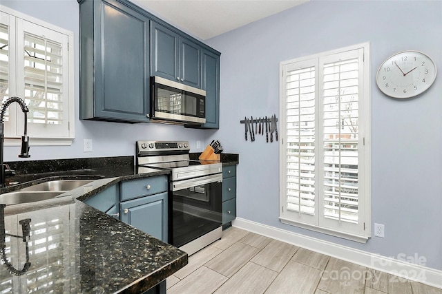 kitchen with stainless steel appliances, blue cabinets, dark stone counters, and sink