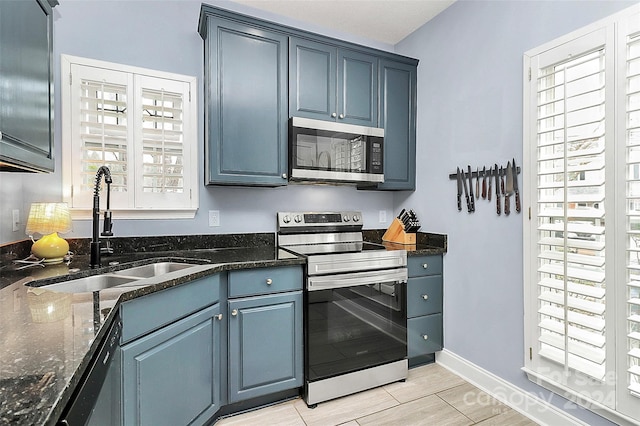 kitchen featuring blue cabinetry, sink, dark stone counters, and appliances with stainless steel finishes