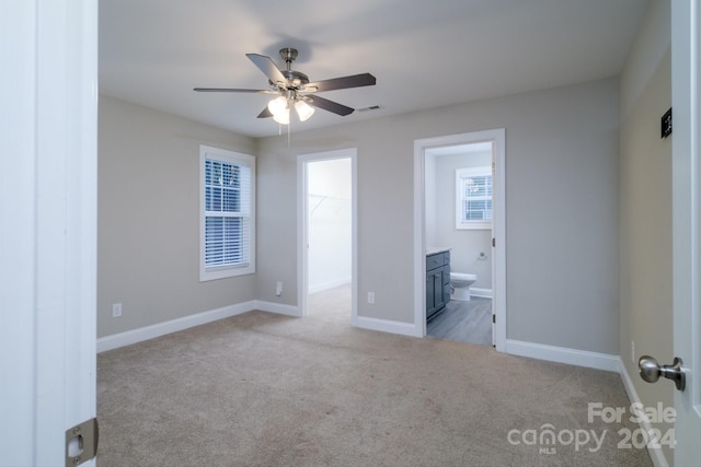 unfurnished bedroom with connected bathroom, ceiling fan, light colored carpet, and a spacious closet