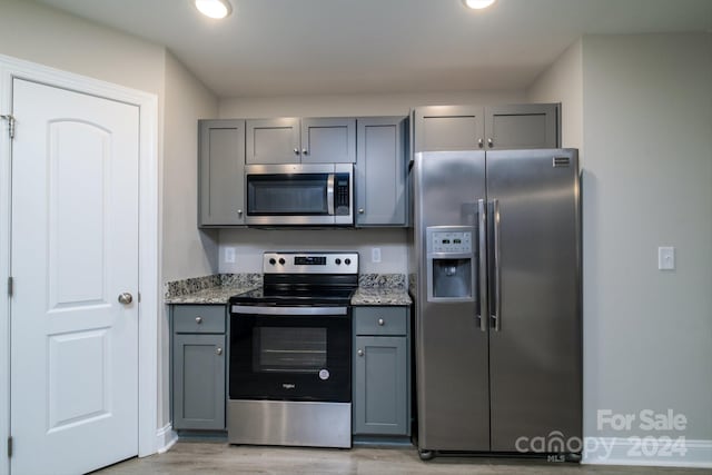 kitchen featuring gray cabinets, light stone countertops, light hardwood / wood-style flooring, and stainless steel appliances