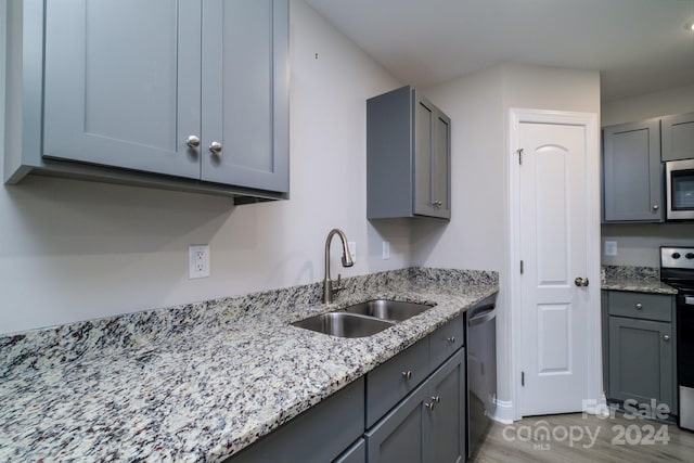 kitchen with sink, light hardwood / wood-style flooring, gray cabinets, light stone countertops, and stainless steel appliances