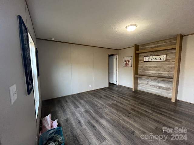 unfurnished bedroom with a textured ceiling, crown molding, dark wood-type flooring, and wooden walls