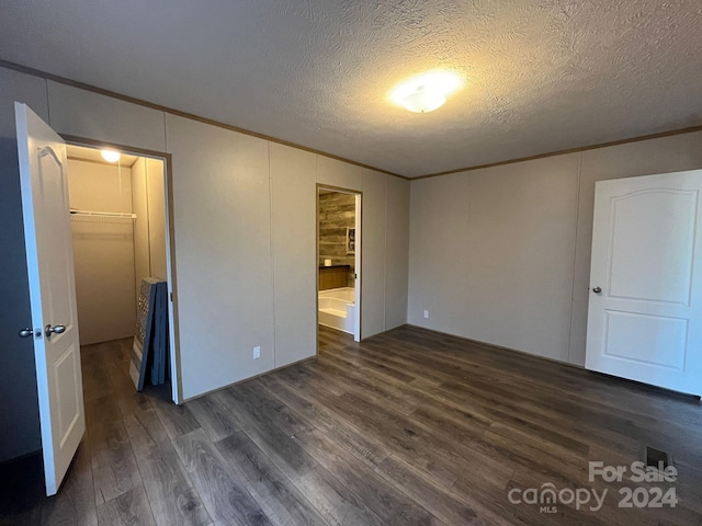 unfurnished bedroom featuring a walk in closet, a textured ceiling, crown molding, dark hardwood / wood-style floors, and a closet