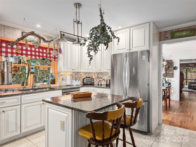 kitchen with dark stone counters, sink, light tile patterned floors, appliances with stainless steel finishes, and a kitchen island