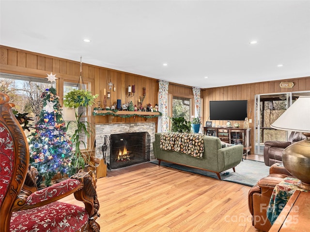 living room with a stone fireplace, wooden walls, wood finished floors, and recessed lighting