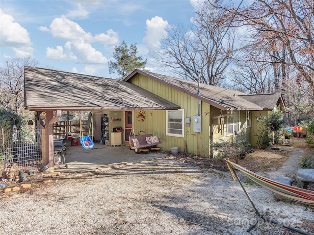 view of front facade featuring a patio, a shingled roof, fence, and an attached carport