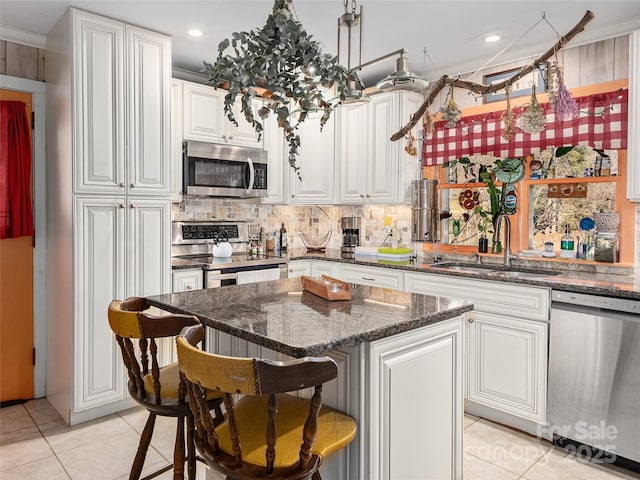 kitchen with white cabinets, stainless steel appliances, a sink, a breakfast bar area, and backsplash