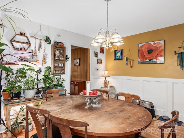 dining room featuring a wainscoted wall, a notable chandelier, and wood finished floors