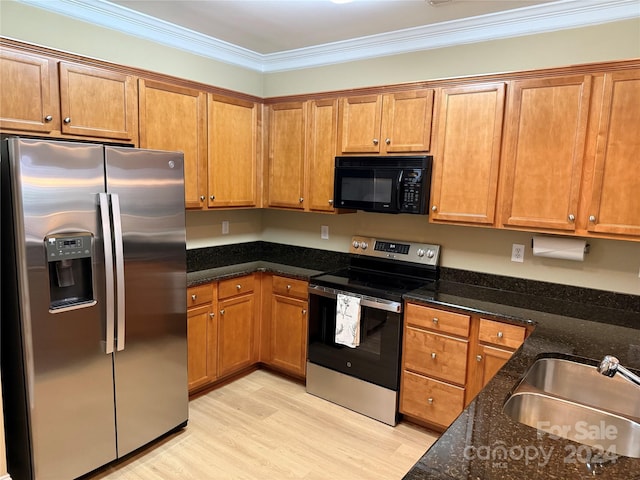 kitchen with appliances with stainless steel finishes, crown molding, sink, light hardwood / wood-style flooring, and dark stone countertops