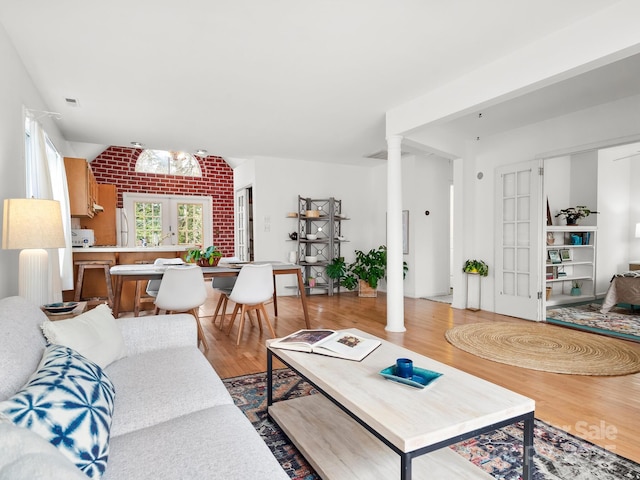 living room featuring light wood-type flooring, french doors, ornate columns, and lofted ceiling