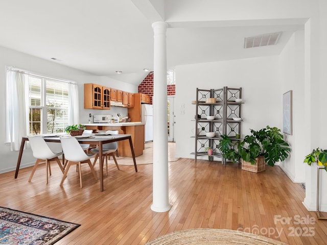 dining space with light hardwood / wood-style floors, vaulted ceiling, and ornate columns