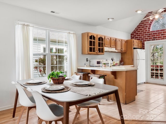 kitchen featuring white appliances, vaulted ceiling, sink, light tile patterned flooring, and kitchen peninsula