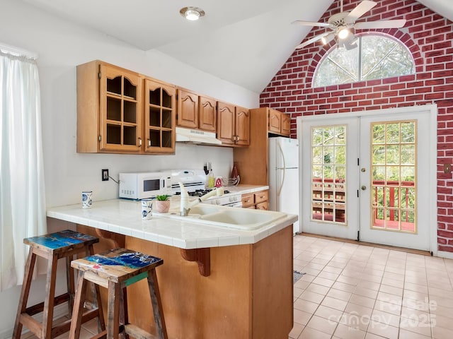 kitchen featuring a breakfast bar area, white appliances, kitchen peninsula, and tile counters