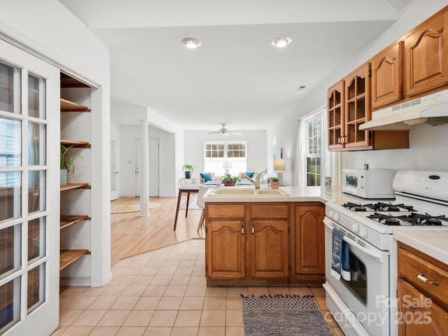 kitchen featuring tile countertops, white appliances, light tile patterned floors, sink, and kitchen peninsula