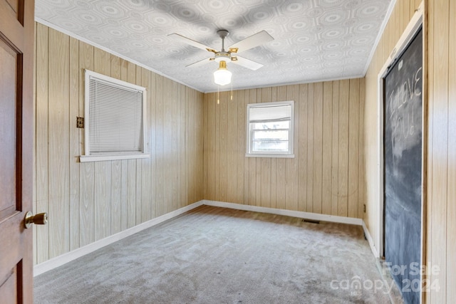 empty room featuring light carpet, ornamental molding, ceiling fan, and wooden walls