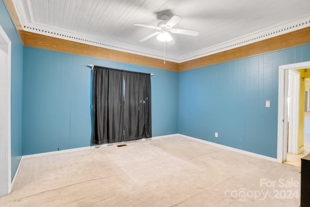 carpeted empty room featuring ceiling fan, wooden walls, and ornamental molding