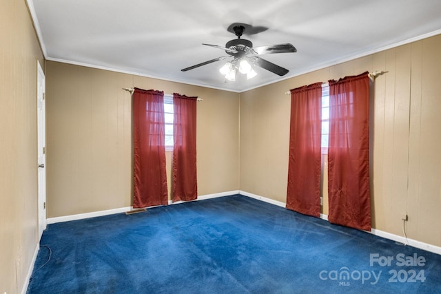 unfurnished room with a wealth of natural light, dark colored carpet, ceiling fan, and ornamental molding