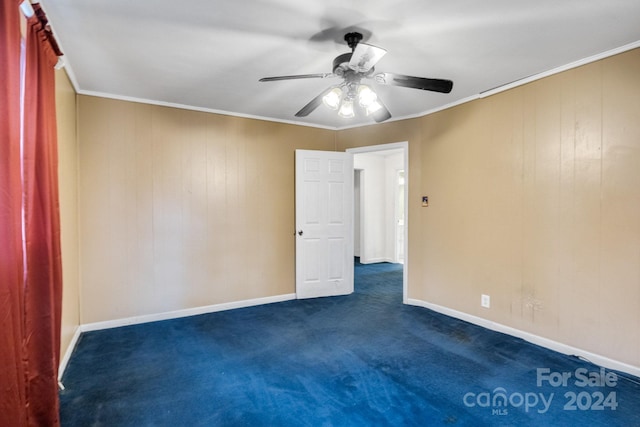 spare room featuring dark carpet, ceiling fan, ornamental molding, and wood walls