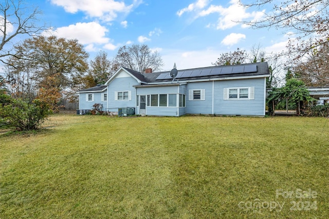 rear view of property featuring central air condition unit, a yard, and solar panels