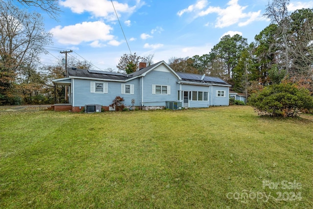 back of property with solar panels, central AC unit, and a lawn