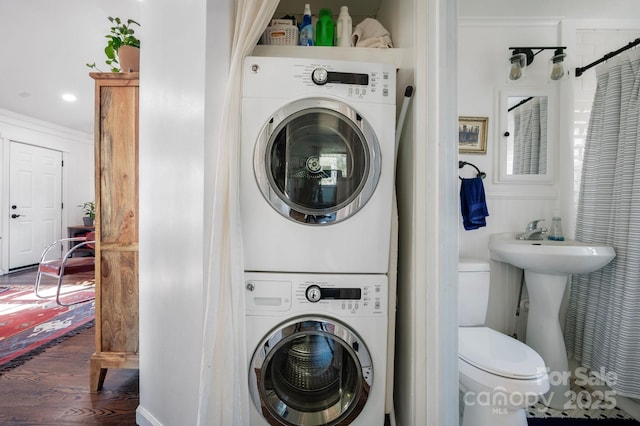 laundry area with stacked washer / drying machine, ornamental molding, and dark wood-type flooring