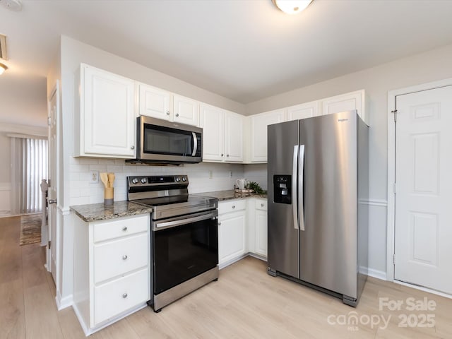 kitchen with white cabinetry, decorative backsplash, stainless steel appliances, and dark stone countertops