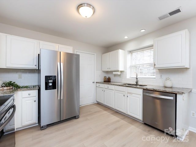 kitchen with sink, appliances with stainless steel finishes, white cabinetry, dark stone countertops, and light wood-type flooring