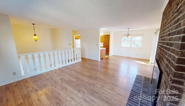 empty room with light hardwood / wood-style flooring, a textured ceiling, and a chandelier