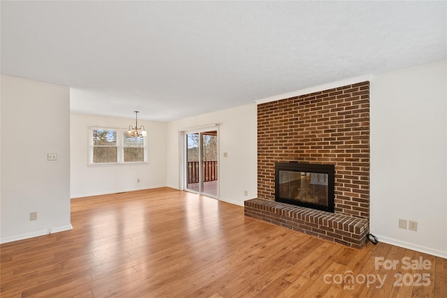 unfurnished living room featuring a textured ceiling, light hardwood / wood-style floors, a fireplace, and a chandelier