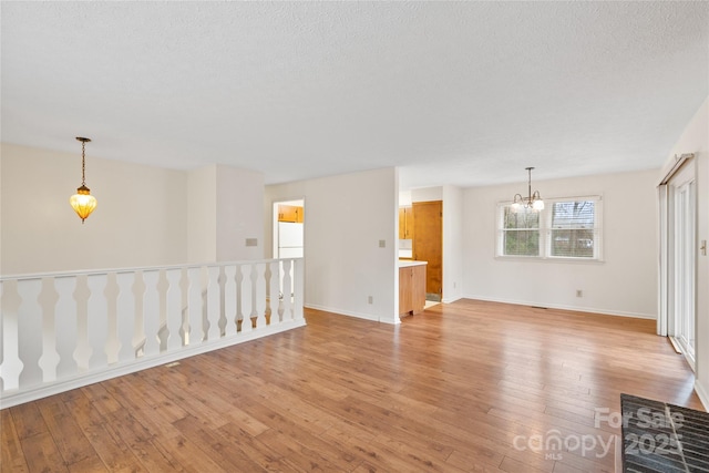 spare room featuring a textured ceiling, light hardwood / wood-style flooring, and an inviting chandelier