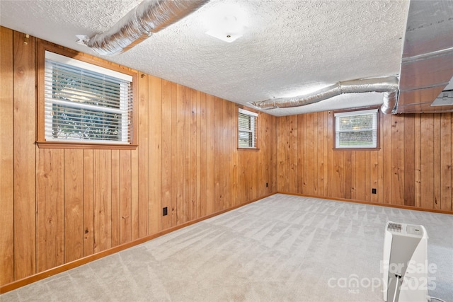 basement featuring wooden walls, plenty of natural light, light carpet, and a textured ceiling