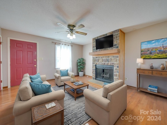 living room featuring a stone fireplace, ceiling fan, a textured ceiling, and light wood-type flooring