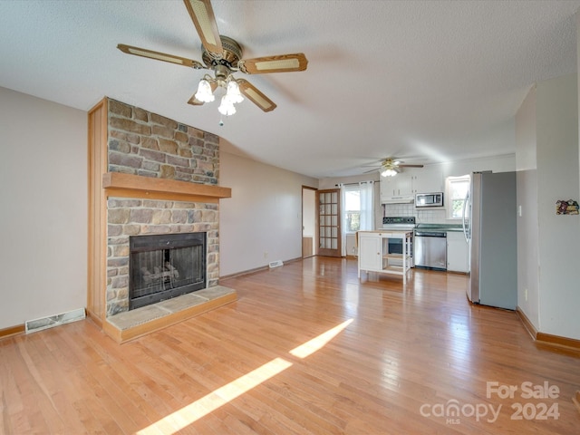 unfurnished living room with ceiling fan, a fireplace, a textured ceiling, and light wood-type flooring