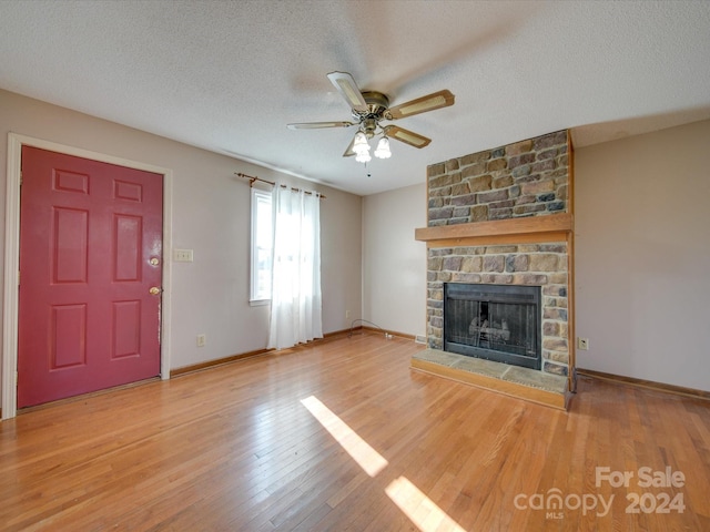 unfurnished living room featuring a stone fireplace, ceiling fan, a textured ceiling, and light wood-type flooring