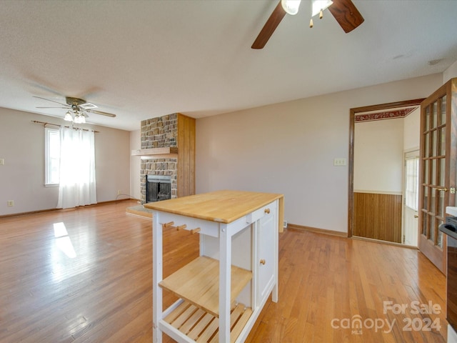 kitchen with wood walls, wooden counters, a stone fireplace, light hardwood / wood-style flooring, and ceiling fan