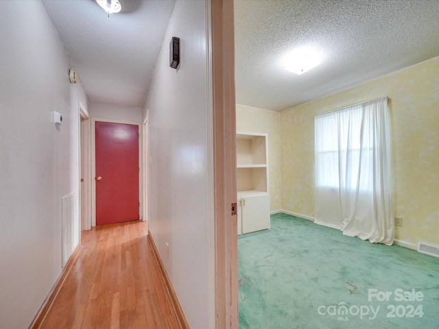 hall with light wood-type flooring and a textured ceiling