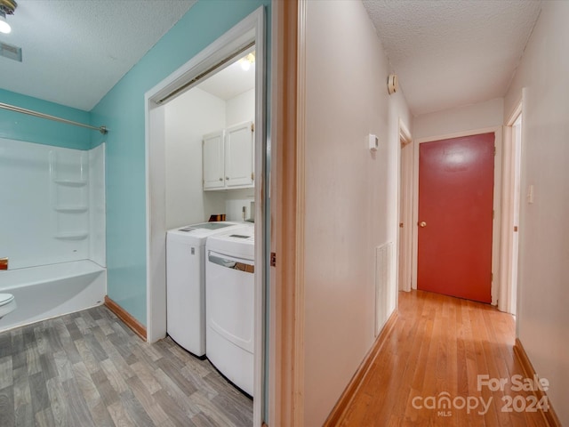 laundry room featuring cabinets, washing machine and dryer, light wood-type flooring, and a textured ceiling