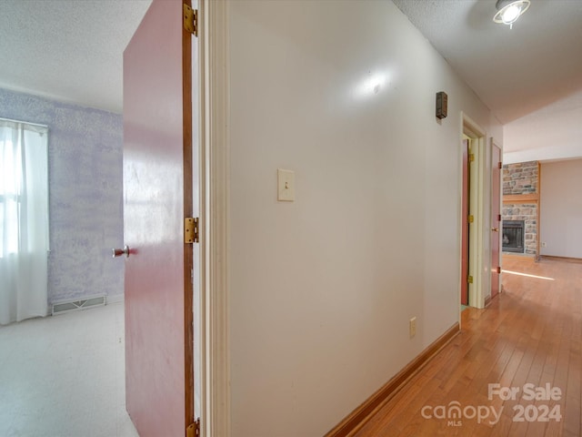 corridor with a textured ceiling and light hardwood / wood-style floors