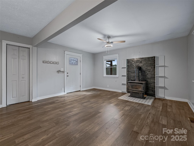 unfurnished living room featuring ceiling fan, a wood stove, a textured ceiling, and dark hardwood / wood-style flooring