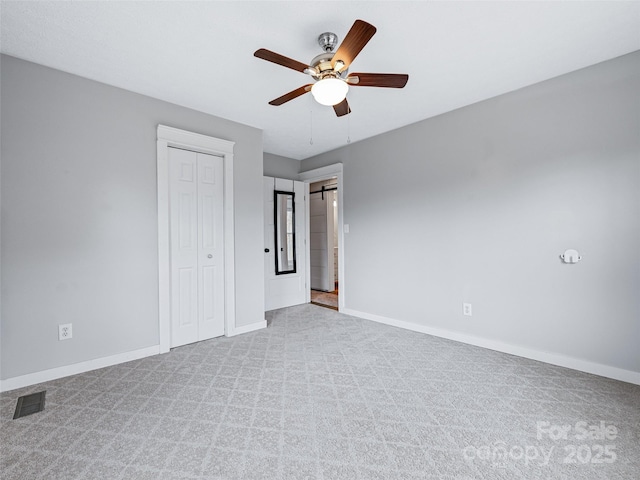 unfurnished bedroom featuring a barn door, light colored carpet, ceiling fan, and a closet