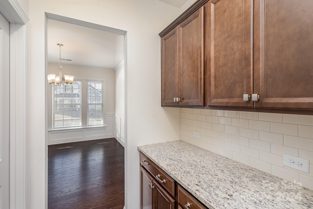 kitchen with backsplash, light stone counters, dark wood-type flooring, and an inviting chandelier