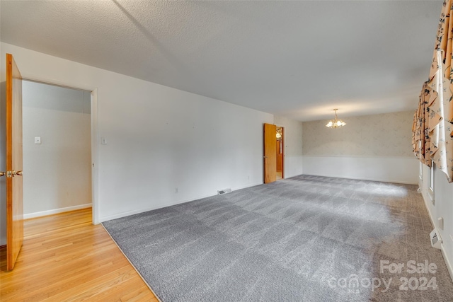 unfurnished room featuring an inviting chandelier, a textured ceiling, and hardwood / wood-style flooring