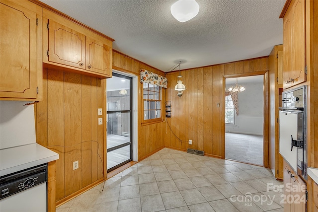 kitchen with pendant lighting, a notable chandelier, dishwasher, black oven, and wood walls