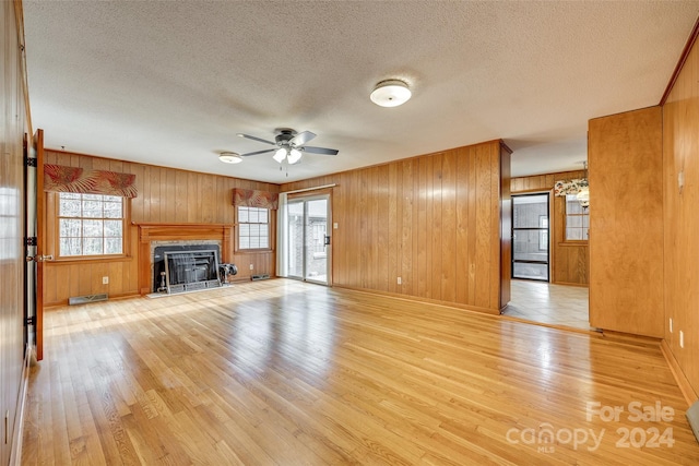 unfurnished living room with wood walls, ceiling fan, light hardwood / wood-style floors, and a textured ceiling